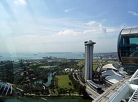 Blick vom Singapore Flyer über eine Gondel am Gipfelpunkt auf die Gardens by the Bay, das Marina Sands Gebäude und den Hafen